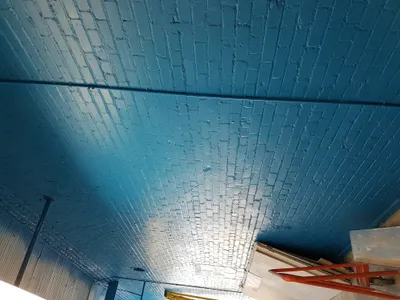 A newly painted teal blue brick ceiling with visible conduit, showcasing a commercial painting project. The brick texture is prominent under the fresh paint.