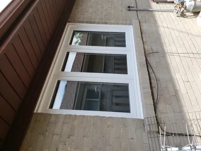 Exterior view of a building facade featuring a newly painted white window frame and trim against a light brown brick wall. Brown siding is visible on the left side of the image.