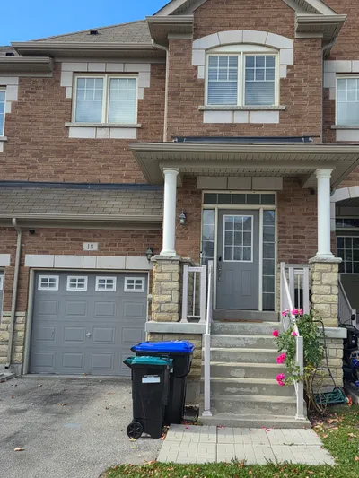 Front exterior of a brick townhouse featuring a newly painted grey garage door and matching grey front entry door. White porch columns and railings frame the entrance, complementing the light-colored window frames and soffit.