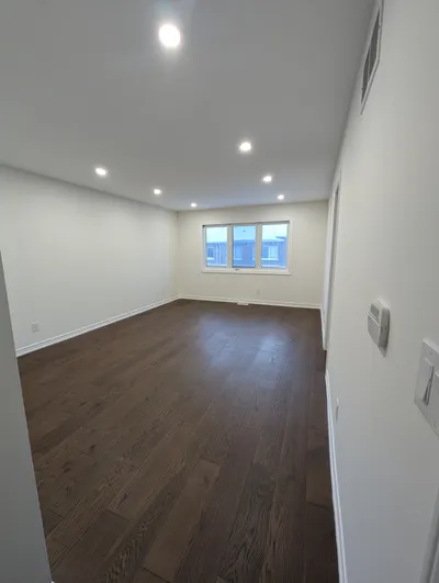 An empty, bright living room after painting, featuring clean white walls, a white ceiling, and crisp white baseboard trim. Dark hardwood floors contrast with the light paint.